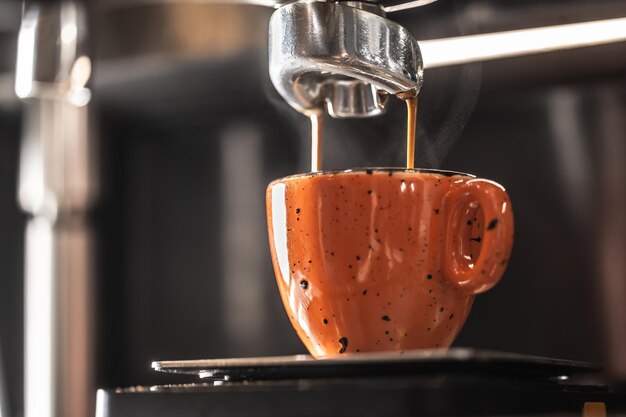 Foto a máquina de café faz café em uma xícara de laranja
