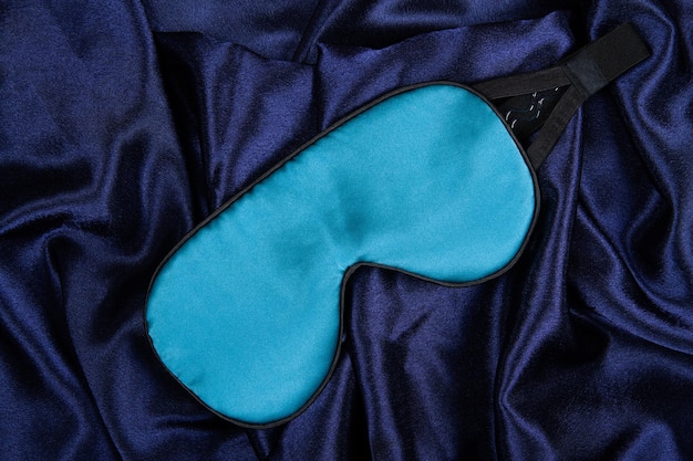A máscara de dormir de seda azul clara está sobre um fundo de seda azul escuro