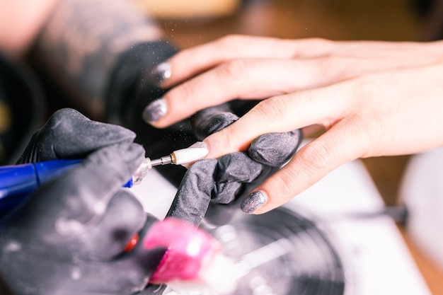 A master feminina usa uma máquina elétrica para remover o esmalte durante a manicure no salão. Perto