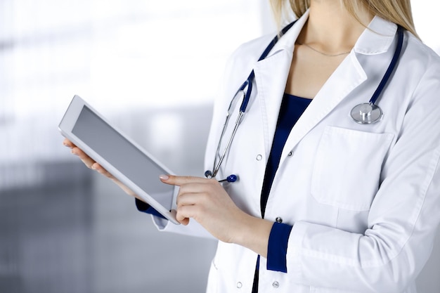 A médica desconhecida está segurando um computador tablet nas mãos, enquanto está em um armário de clínica. Médica no trabalho, close-up. Serviço médico perfeito em um hospital. Conceito de medicina.