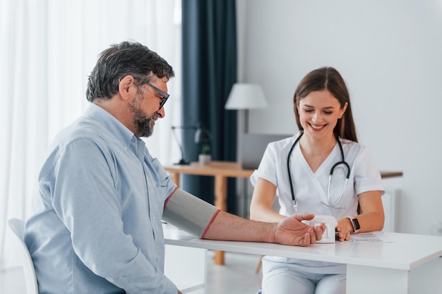 A médica está a medir a pressão arterial do homem. Um médico profissional de casaco branco está no escritório.