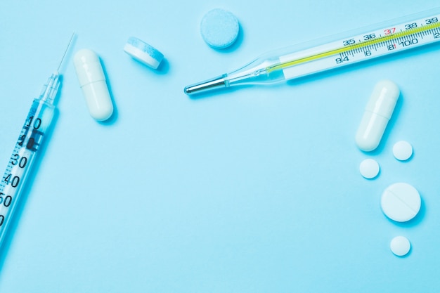 A medicina de seringa e termômetro médico na cor azul pastel