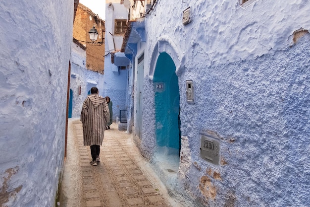 A medina de Chefchaouen em Marrocos Um homem vestindo o tradicional casaco berbere caminha por uma rua