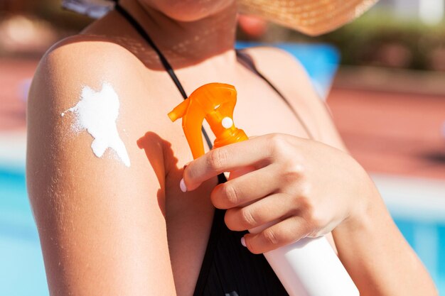 A menina a aplicar creme protetor solar ao seu corpo conceito de saúde e medicina