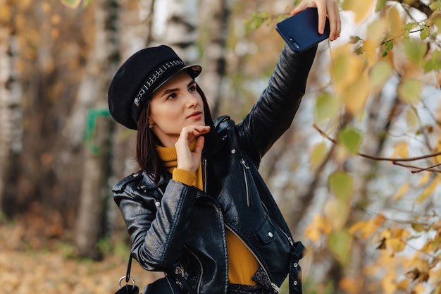 A menina à moda elegante acolhedor no parque colorido do outono faz fotos