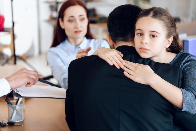 A menina abraça o homem no terno que senta-se oposto à mulher.