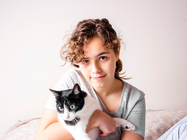 Foto a menina adolescente encaracolado bonita na cama abraça seu gato