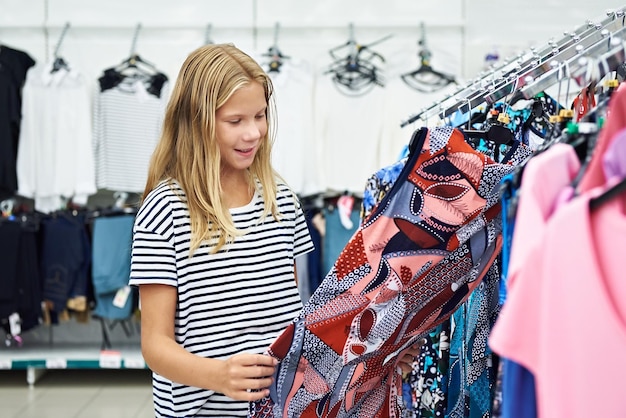 A menina adolescente escolhe o vestido na loja