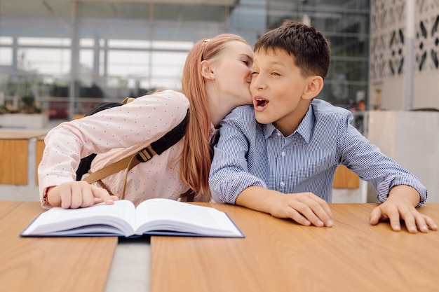 A menina adolescente está sussurrando algo no ouvido do menino ou beijando-o