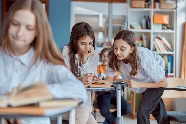 A menina ajuda a ler seu colega de classe. Crianças do ensino fundamental sentadas em mesas e lendo livros em sala de aula.