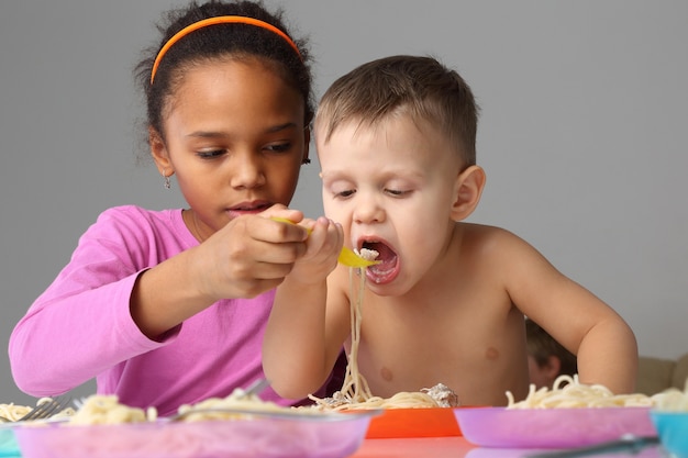 A menina ajuda o bebê a comer espaguete