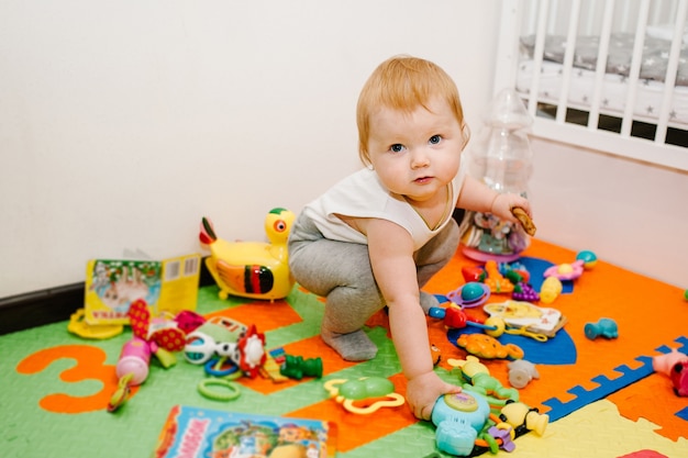 A menina alegre mostra e joga muitos brinquedos no tapete colorido e quebra-cabeças