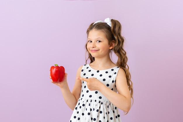 A menina aponta para a pimenta vermelha com o dedo indicador Legumes para a saúde das crianças