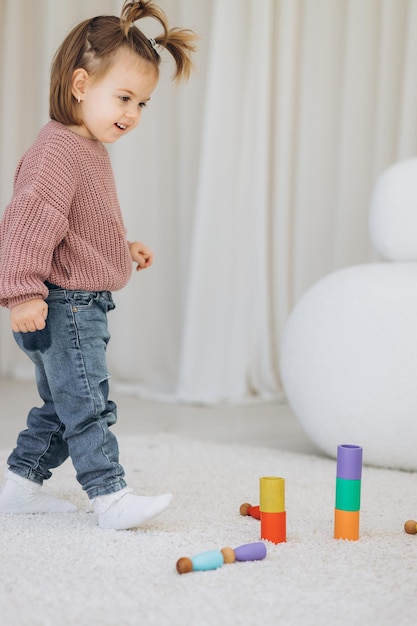 A menina aprende as cores brincando com figuras humanas coloridas de brinquedos cilíndricos de madeira e colocando-as em copos da cor apropriada a criança fica feliz por ter concluído a tarefa corretamente