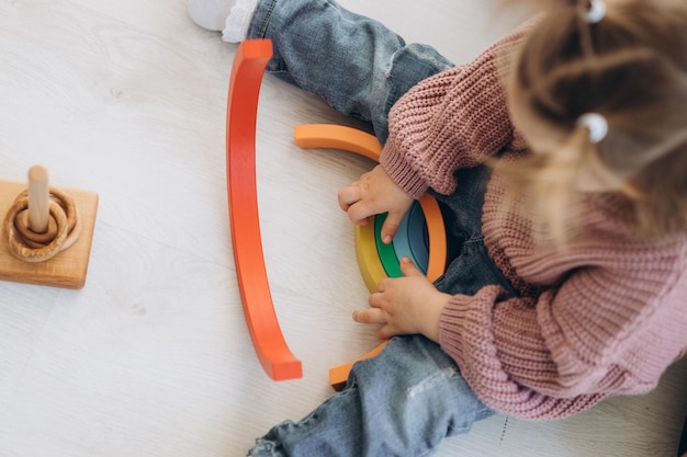 A menina aprende as cores brincando com figuras humanas coloridas de brinquedos cilíndricos de madeira e colocando-as em copos da cor apropriada A criança fica feliz por ter concluído a tarefa corretamente