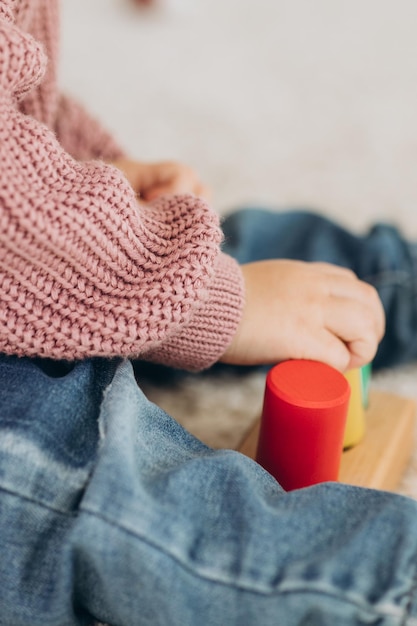 A menina aprende as cores brincando com figuras humanas coloridas de brinquedos cilíndricos de madeira e colocando-as em copos da cor apropriada A criança fica feliz por ter concluído a tarefa corretamente