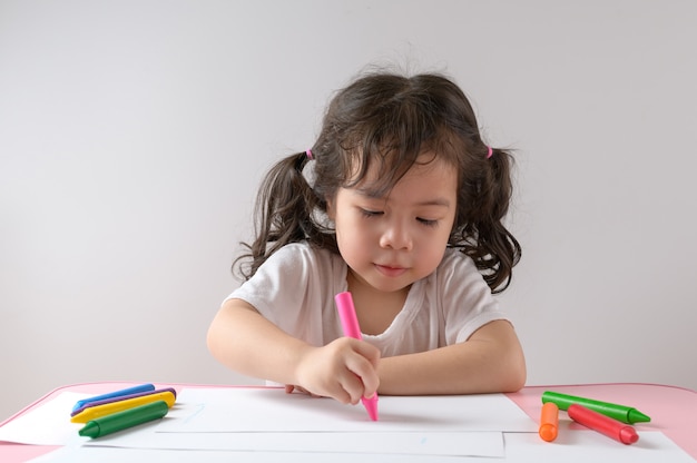 A menina asiática encaracolada pequena gosta de desenhar em casa. Conceito de educação.