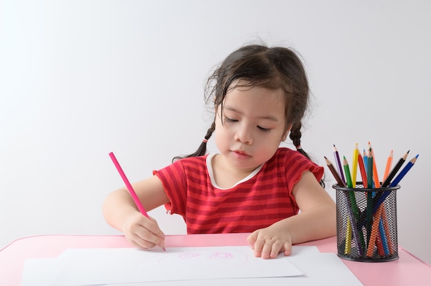 A menina asiática encaracolada pequena gosta de desenhar em casa. Conceito de educação.