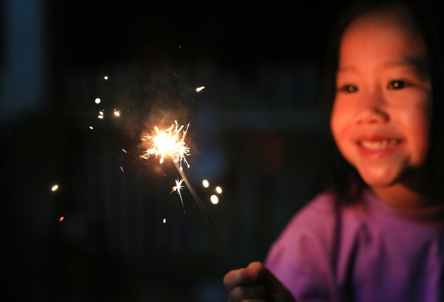 A menina asiática pequena da criança aprecia jogar foguetes. Concentre-se em fogos de fogo.