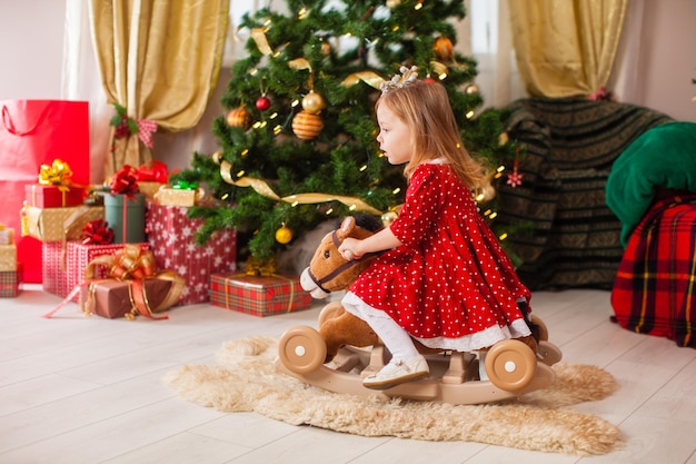 A menina balança no brinquedo do cavalo de balanço na sala decorada de Natal