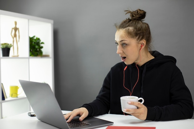 A menina bonita agradável olha surpreso para o laptop, verifique as lojas on-line para vendas