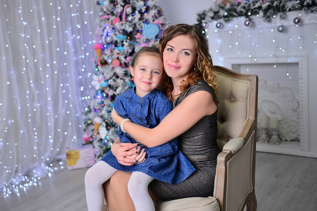 A menina bonita com a mãe está decorando uma árvore de natal na casa