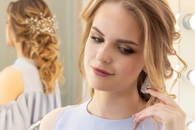 A menina bonita com um penteado de casamento se olha no espelho, retrato de uma jovem garota. maquiagem linda.