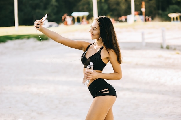 A menina bonita do cabelo escuro do lond no sportwear na praia faz o selfie