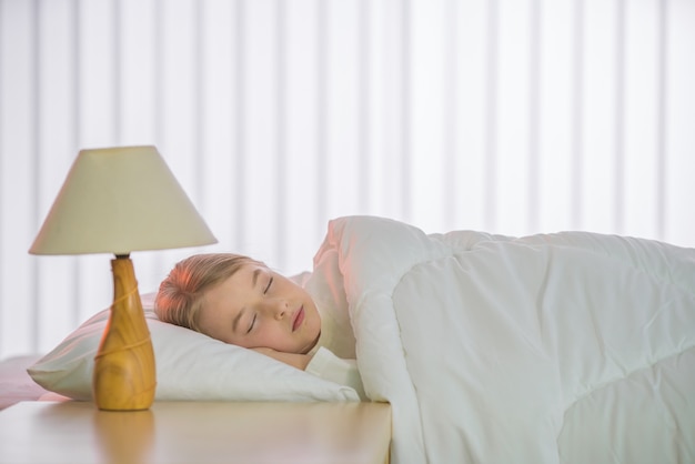 A menina bonita dormindo na cama com lençóis brancos