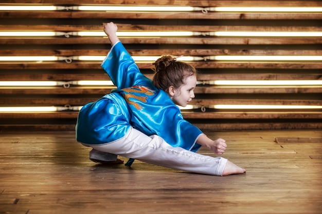A menina bonita na sala em roupas esportivas para artes marciais é Wushu ou kung fu
