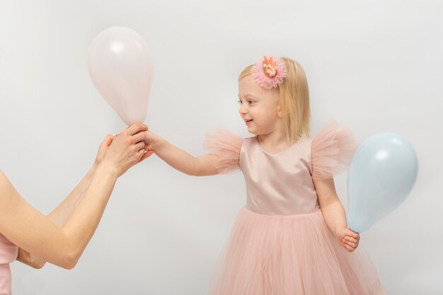 A menina bonita no vestido cor-de-rosa exuberante que sorri toma o balão das mãos da mulher Princesinha loura isolada no fundo branco
