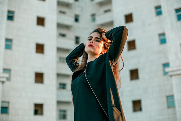 Foto a menina bonita nova em um revestimento preto levanta perto de uma casa branca alta.