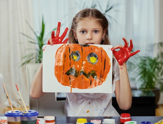 A menina bonitinha tem um pôster com abóbora de Halloween pintada.