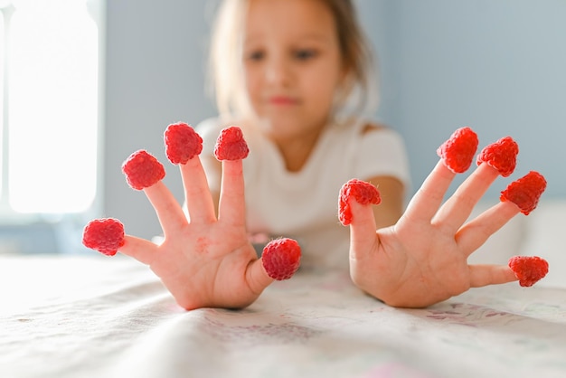 A menina brincava com framboesas nos dedos