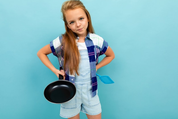 A menina caucasiano do adolescente está indo fritar algo com uma panela isolada no fundo azul