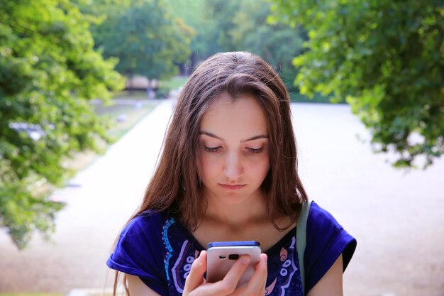 A menina com um telefone celular lê a mensagem no parque