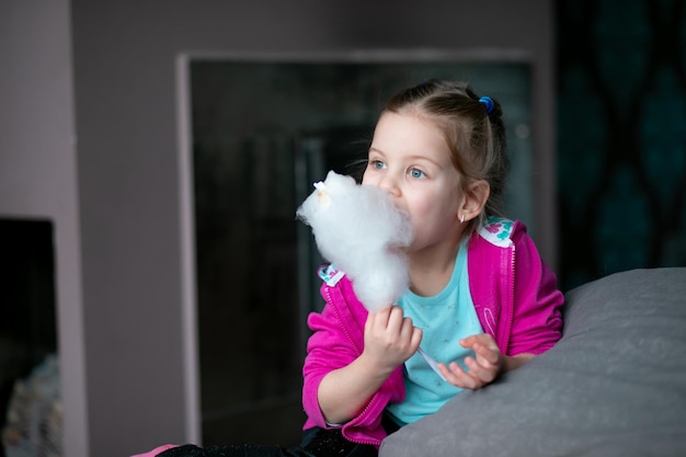 Foto a menina come algodão doce em casa, feliz jardim de infância, morde algodão doce, doces favoritos su