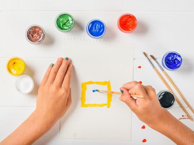 A menina começa a pintar a casa em uma folha de papel em uma mesa branca.