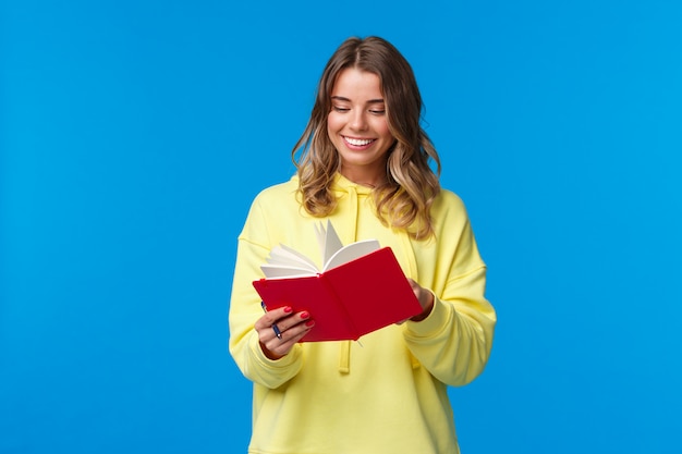 A menina comprou o planejador novo, anotando notas ou palestra, sorrindo alegremente, segurando o caderno vermelho, decida iniciar diário secreto, parado no capuz amarelo