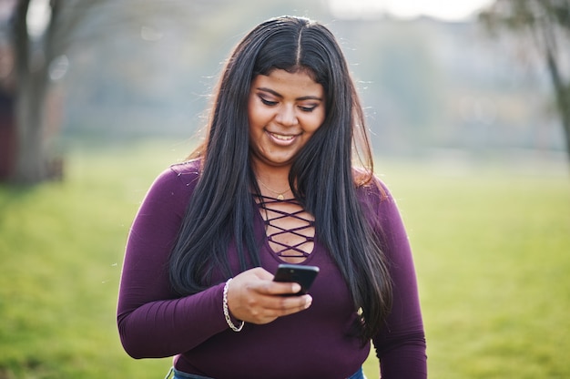 A menina consideravelmente latino do modelo xxl do Equador veste a blusa violeta levantada na rua e olhando no telefone móvel.