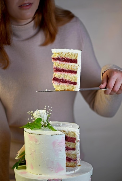 A menina corta e serve um pedaço de bolo de casamento festivo bolo de duas camadas decorado com flores frescas em um fundo cinza