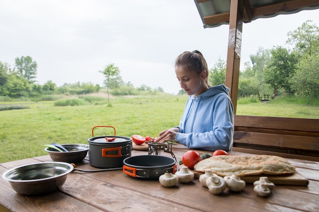 A menina corta tomates em uma placa de madeira no acampamento