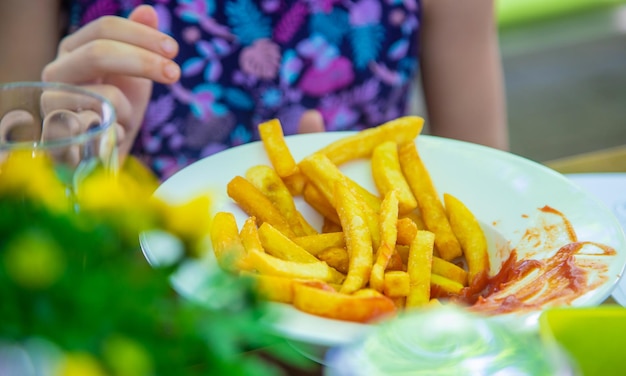 A menina da criança come o foco seletivo das batatas fritas