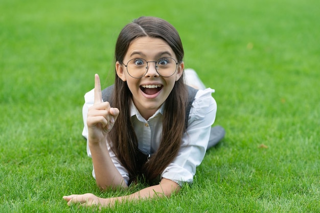 A menina da escola feliz teve a ideia de manter o dedo levantado deitado na grama Ideia genial e eureka