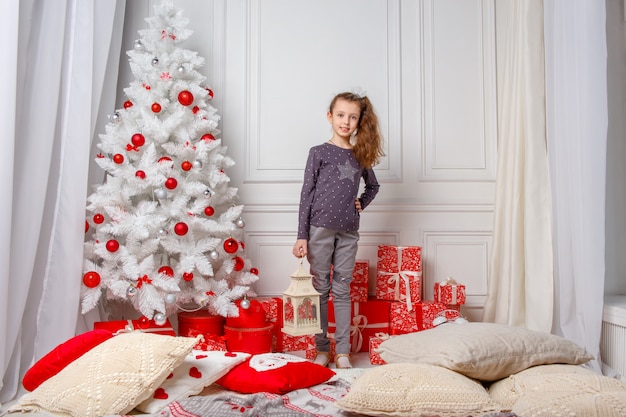 A menina de cabelos compridos branca decora uma sala com brinquedos do natal. uma menina e uma árvore de natal