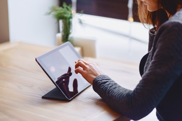 A menina de óculos limpa a tela do tablet na mesa de closup