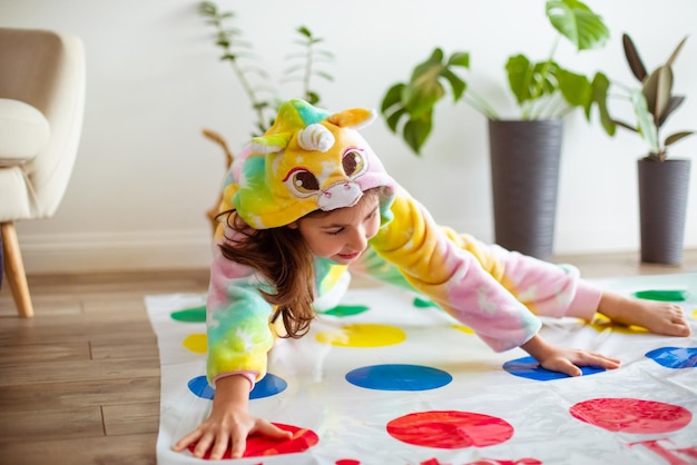 A menina de pijama de unicórnio está jogando o jogo twister A menina está jogando ativamente na sala