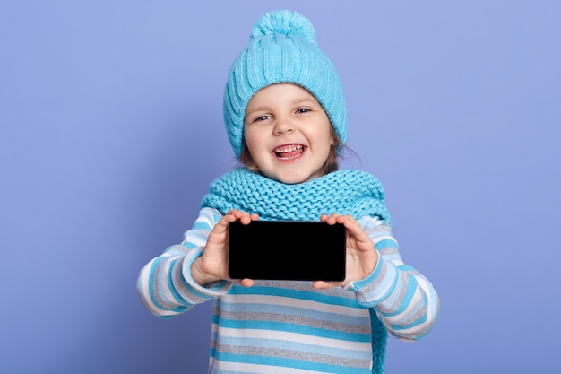 A menina de sorriso da criança veste o chapéu moderno do inverno