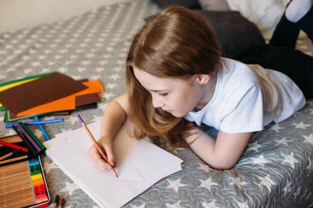 A menina depois da escola brinca em casa, desenha com lápis e canetas.