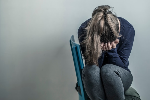 A menina depressiva e desesperada senta-se em uma cadeira. Mulher jovem triste. Copie o espaço.